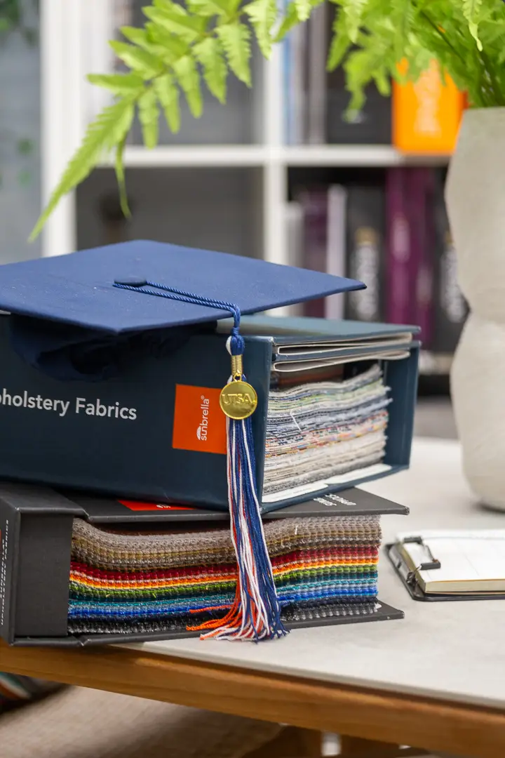 Still life of a graduation cap and tassel resting on a stack of upholstery fabric binders.