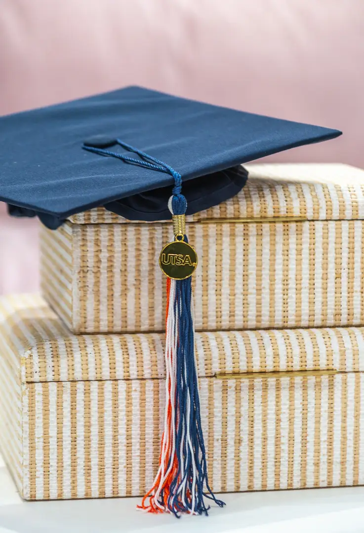 Still life of a graduation cap and tassel resting on a stack of striped upholstered boxes.