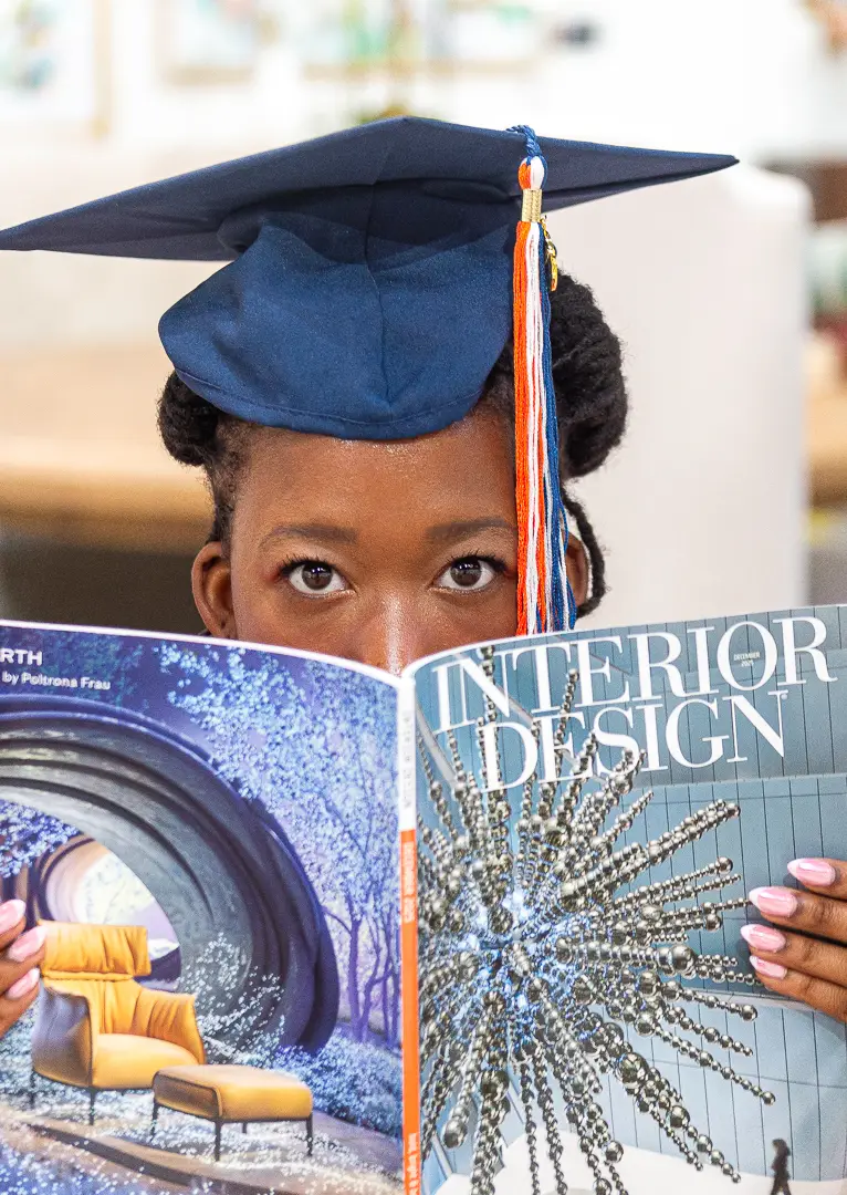 Graduate wearing her cap and peeking over the top of an Interior Design magazine.