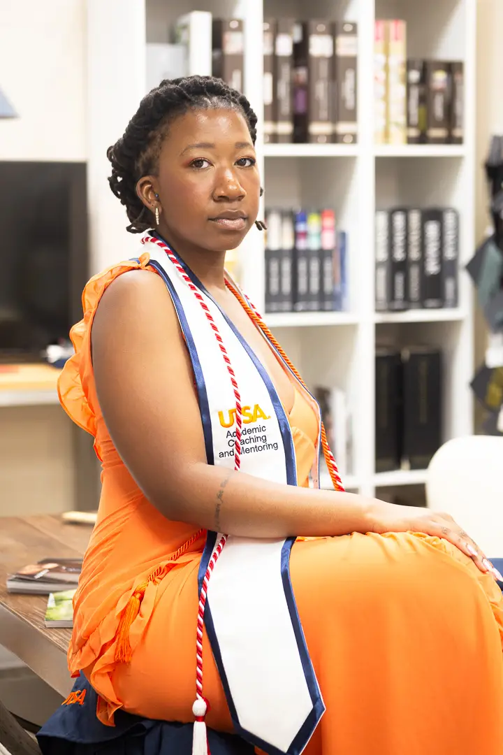 Seated three quarter portrait of a graduate wearing a UTSA stole, photographed in front of a bookshelf.