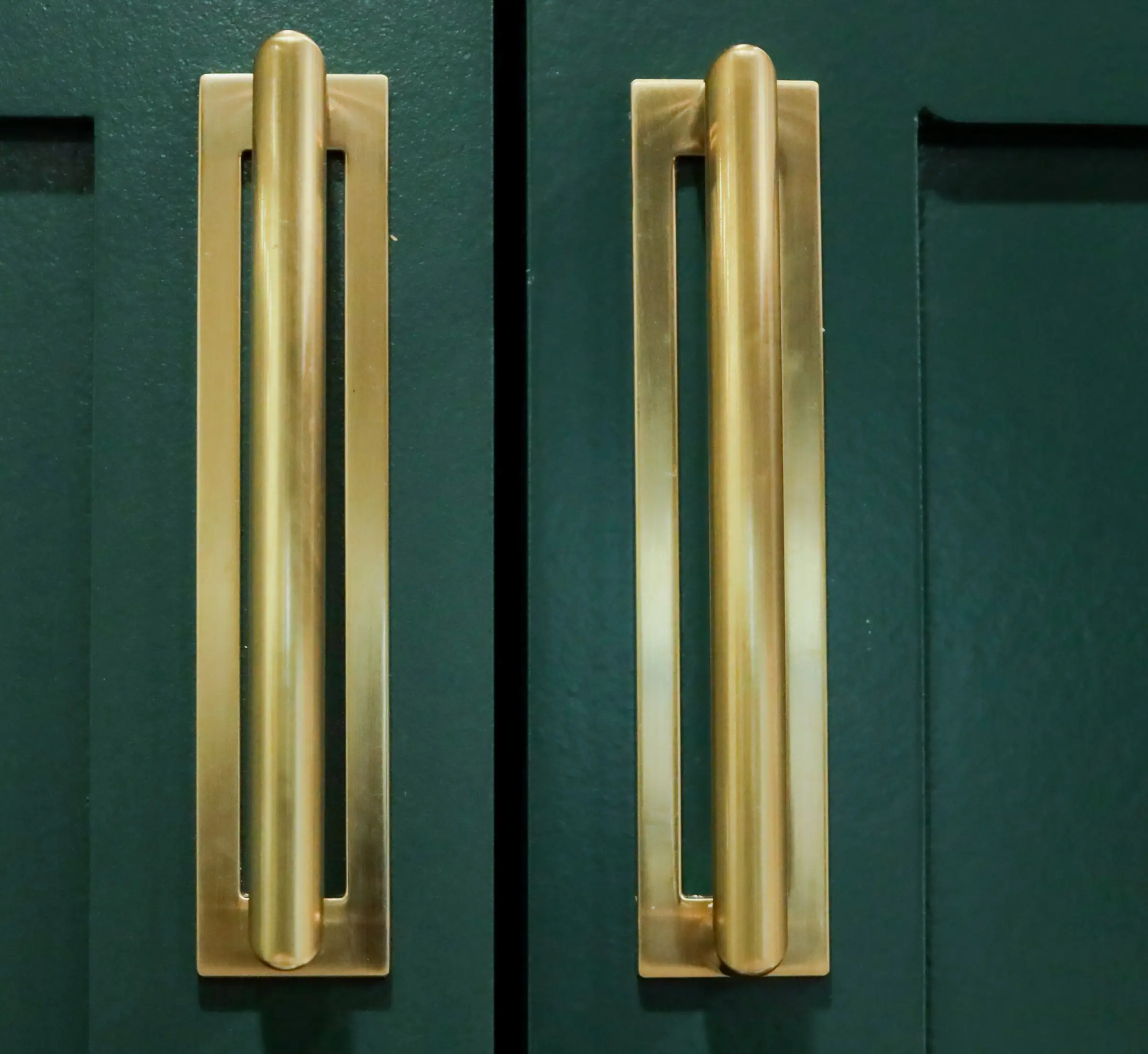 Interior design detail shot of matching brass cabinet pulls on dark green cabinetry.