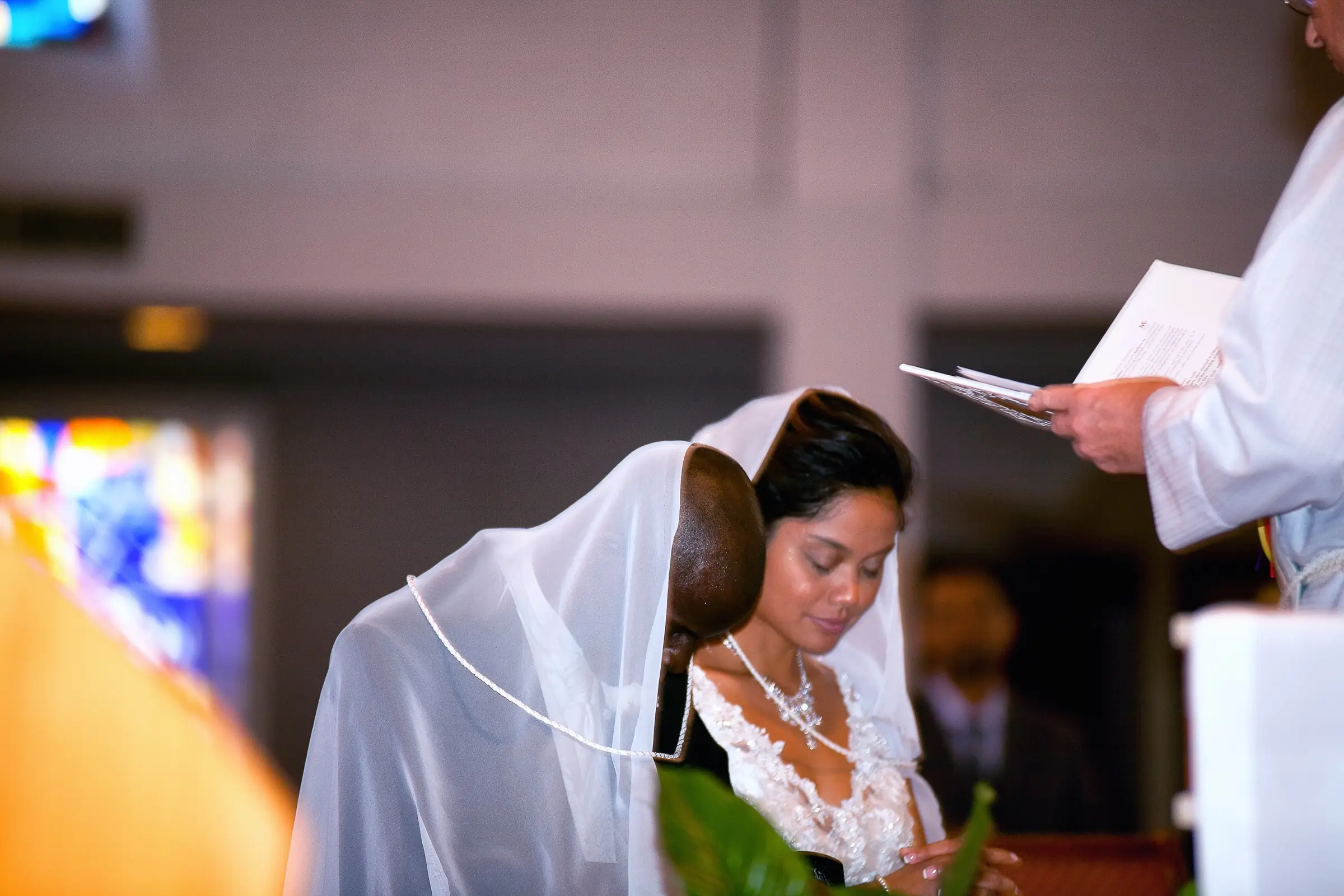 Candid moment of a bride during a wedding ceremony, veil catching the light.